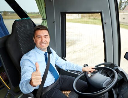 transport, tourism, road trip and people concept - happy driver driving intercity bus and snowing thumbs up